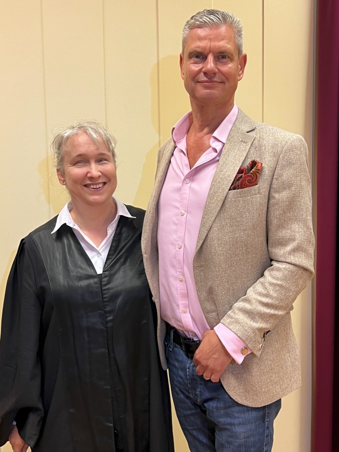 Pamela Pabst links, Ingo Hoppe rechts, beide stehend, in Richtung Kamera blickend, vor weißen Paneelen mit weinrotem Vorhangsaum am rechten Rand